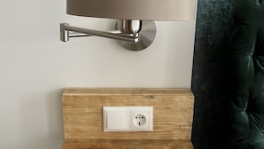 A wall-mounted lamp with a cylindrical shade, a wooden shelf below it, and a power outlet. - Live in the center, enjoy peace and quiet (Greifswald)