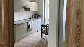 A modern kitchen with white cabinets, a wooden floor, and a dining area with a table and chairs. - Live in the center, enjoy peace and quiet (Greifswald)
