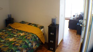 Un dormitorio con una cama, una mesita de noche, una lámpara y vistas a una sala de estar con un sofá.