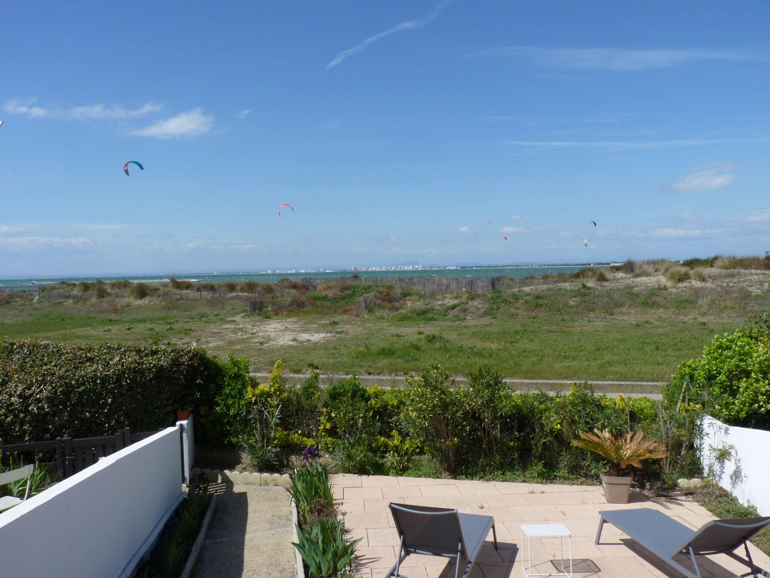 En terrasse med to liggestole og et bord, med udsigt over en strand med klitter og en klar himmel.