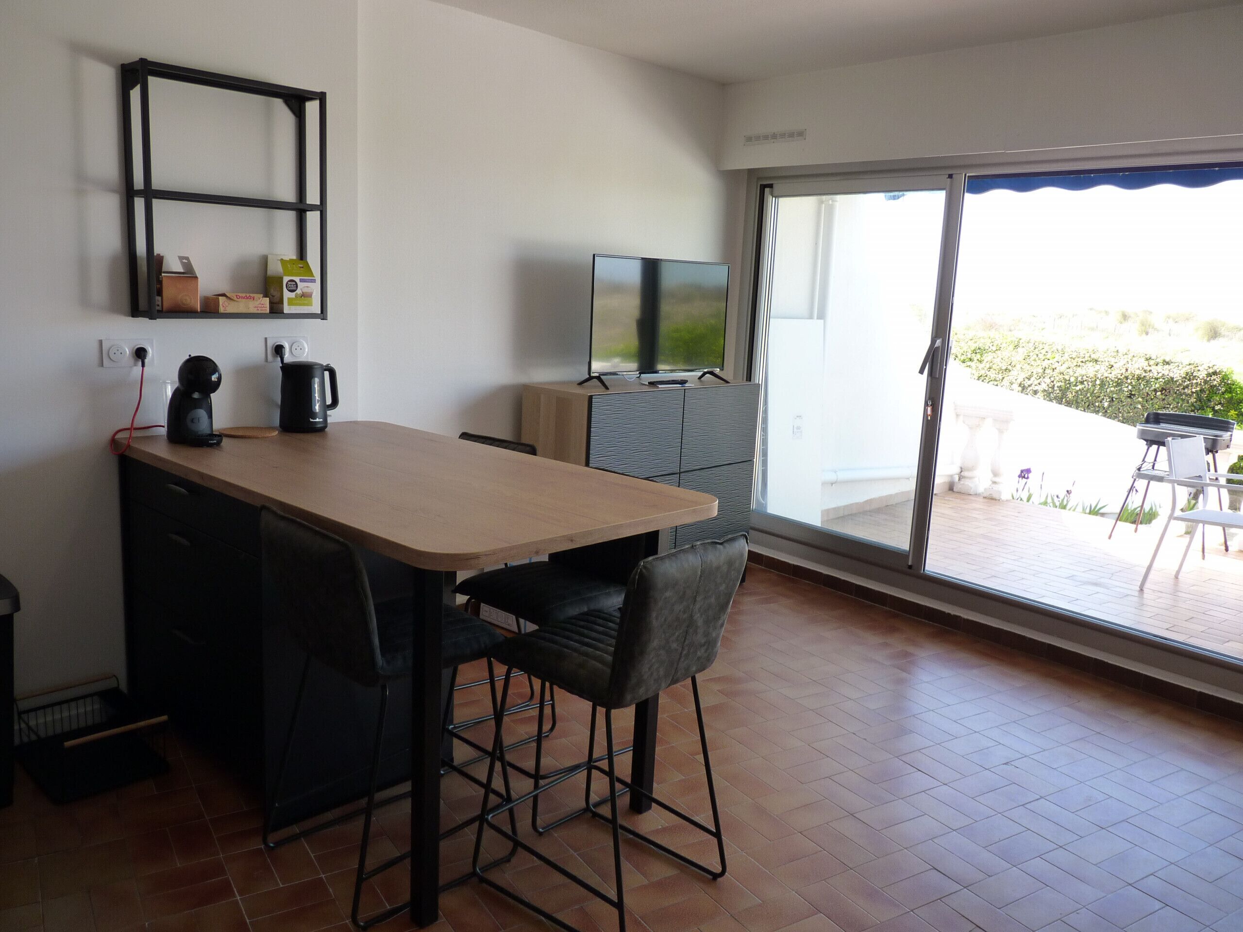 Una cocina moderna con encimera de madera, sillas negras, un televisor y una puerta corrediza de vidrio que da a un patio exterior.