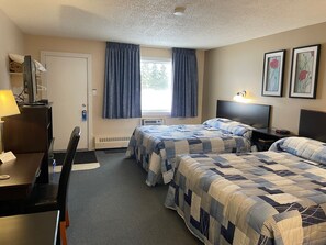 A hotel room with two beds, a desk, a chair, a window with curtains, and a radiator. - Shellbrook Motel (Shellbrook)