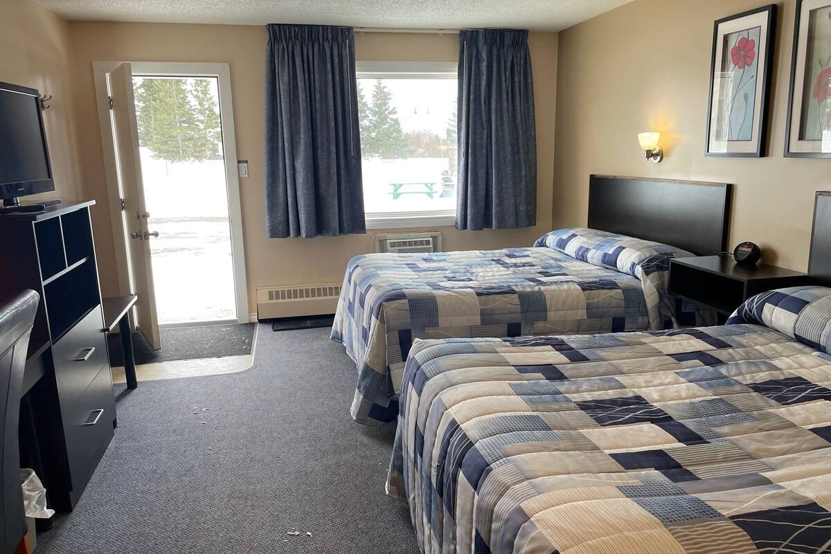 Quarto de hotel com duas camas, uma escrivaninha, uma televisão e uma janela com cortinas.