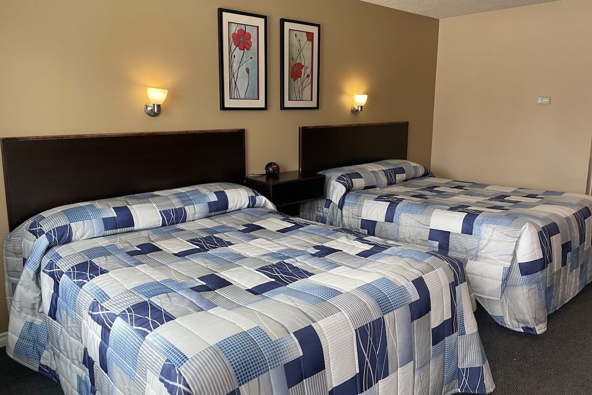 Quarto de hotel com duas camas, cada uma com colcha acolchoada azul e branca, cabeceira escura e duas luminárias fixadas na parede.
