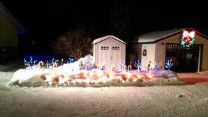 Een huis met garage en tuinhuis, omringd door sneeuw en verlicht met kleurrijke lampjes.