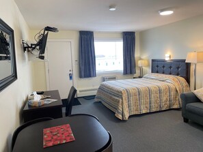 A hotel room with a bed, a desk, a chair, a lamp, and a window with curtains. - Shellbrook Motel (Shellbrook)