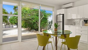 A modern kitchen with white cabinets, a stainless steel refrigerator, and a glass dining table with yellow chairs. - Boca Catalina Beach 1 Bed/Kitchen Private Pool (Noord)