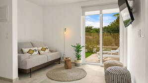 A modern living room with a grey sofa, a round rug, a wooden stool, and a potted plant. - Boca Catalina Beach 1 Bed/Kitchen Private Pool (Noord)