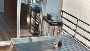 Une boîte de rangement en osier avec un couvercle en métal, placée sur un balcon doté d’une rambarde en métal et d’une porte en verre en arrière-plan.