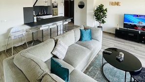 Un salon moderne avec un grand canapé d’angle gris, une table basse ronde et un téléviseur posé sur un meuble noir.