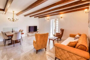 Un salon moderne comprenant un canapé, des fauteuils, une table à manger avec des chaises, un téléviseur et un lustre.