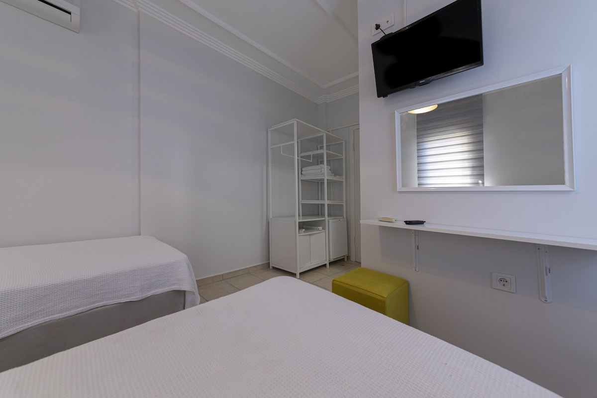 Habitación de hotel con dos camas, un armario, televisor montado en la pared y una ventana con persianas.
