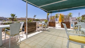 Un patio al aire libre con sillas y mesas de mimbre blanco, un dosel verde y vistas del paisaje.