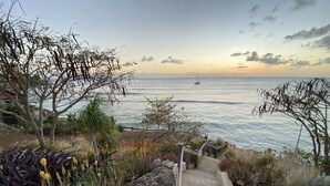 A coastal pathway leading to a beach with a sailboat in the distance. - Searocks Beach Apartment (Oistins)