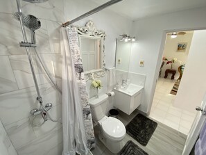 A bathroom with a shower, toilet, sink, and a mirror. - Searocks Beach Apartment (Oistins)