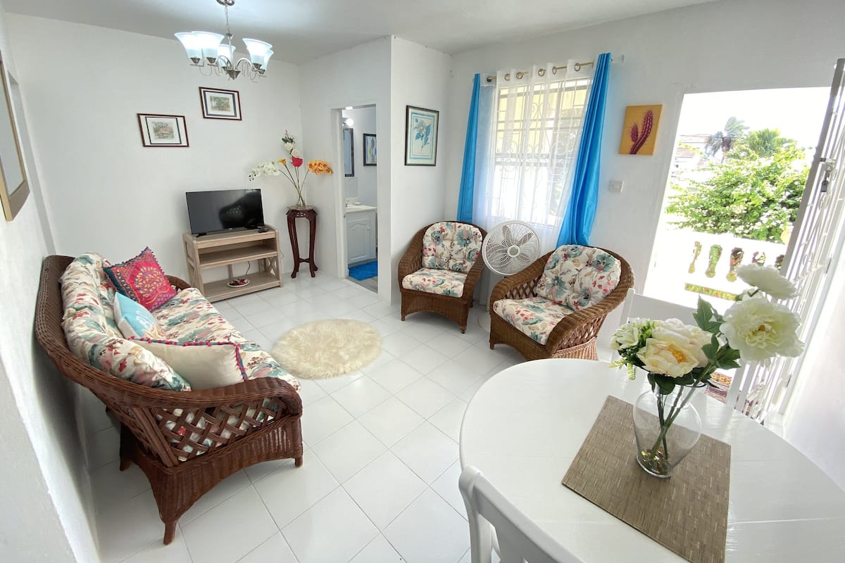 A living room with a sofa, two armchairs, a TV, a fan, and a table with a vase of flowers.