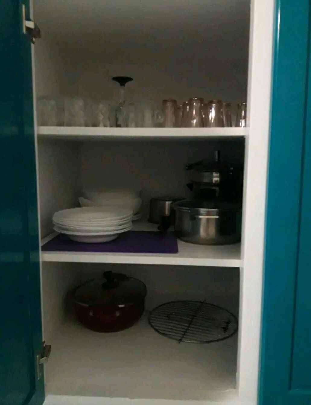 A kitchen with shelves holding plates, a pot, and a grill.