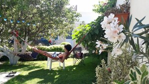Eine Person entspannt in einer Hängematte in einem üppigen Garten mit verschiedenen Pflanzen und Blumen.