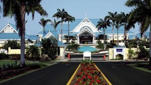 A resort entrance with a central gate, palm trees, and a blue-roofed building. - Magdalena condo (Lowlands)
