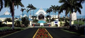 A resort entrance with a central gate, palm trees, and a blue-roofed building. - Magdalena condo (Lowlands)