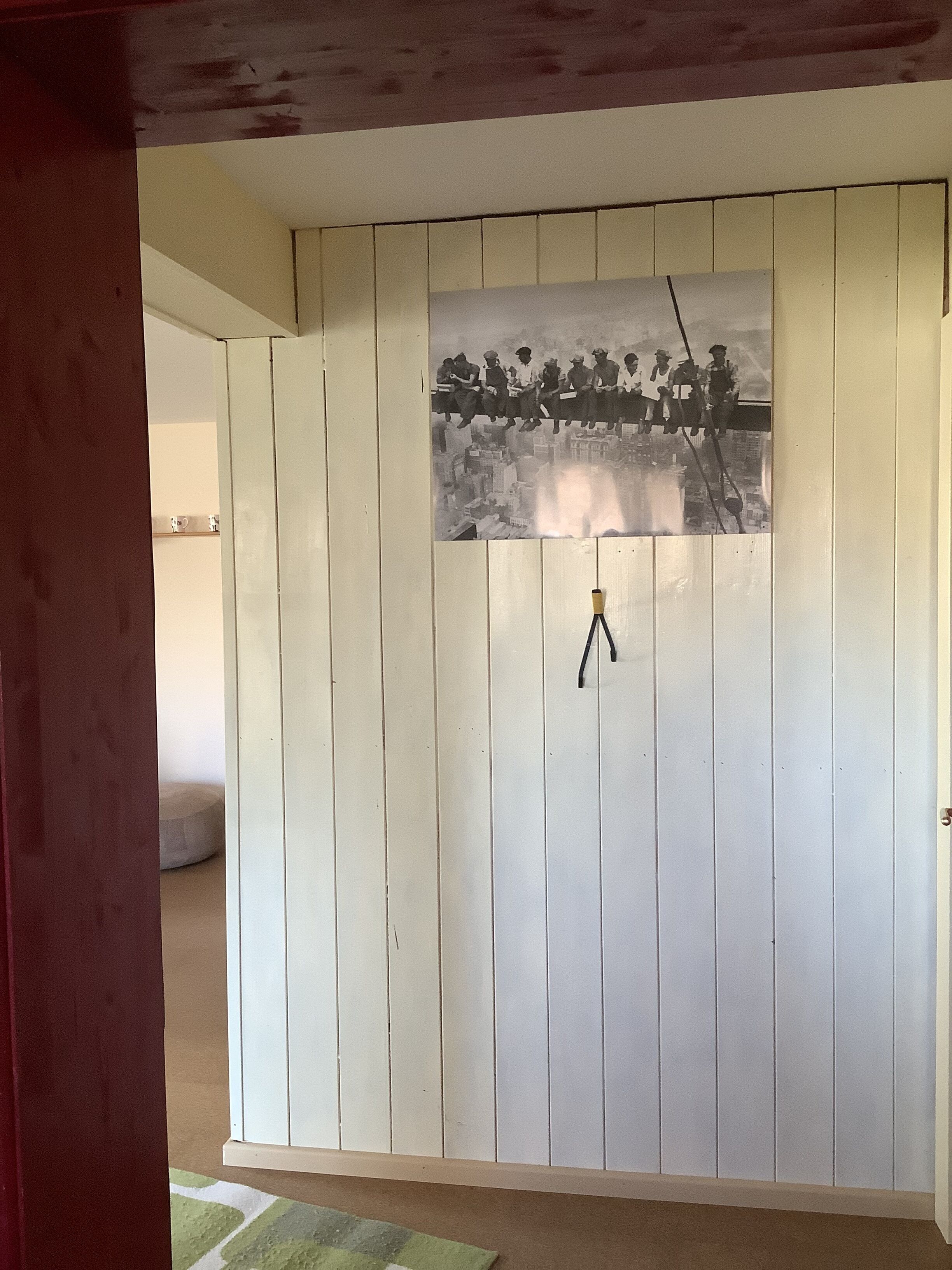 A room with a white wooden wall, a mounted picture of a historical event, and a tripod in the center.
