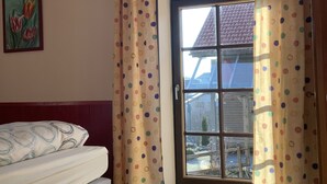 Ein Schlafzimmer mit Bett, einem Vorhangfenster, einem Wandbild und Blick ins Freie.
