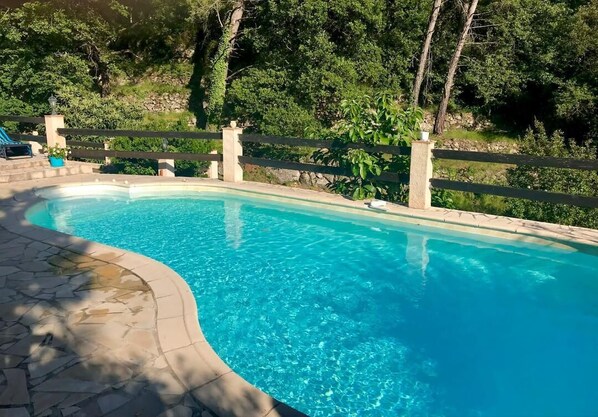 Uma piscina com borda de pedra, rodeada por um cercado de madeira e vegetação exuberante.