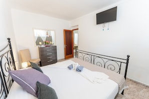Ein Schlafzimmer mit einem Bett, einem Schminktisch, einem Spiegel, einem Fernseher und einer Tür.