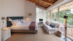 Un dormitorio con cama, mesita de noche, lámpara, televisor, sofá y ventanas amplias.