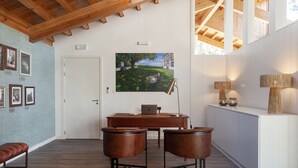 Un interior moderno con techo de madera, un escritorio con dos sillones de cuero, un cuadro de paisaje y un armario blanco con una lámpara.