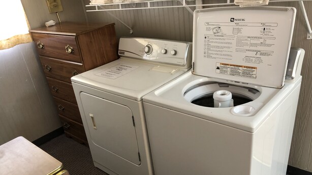 A compact laundry area with a front-loading washer and dryer, a wooden dresser, and a small table with a tissue box.