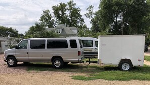 A silver van with a white trailer attached, parked on a gravel driveway.
