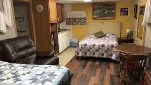 A room with two beds, a wooden chair, a small table, a sink, and a clock.