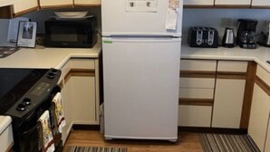 Pieni, käytännöllinen keittiö, jossa on valkoinen jääkaappi, mikroaaltouuni, leivänpaahdin ja kahvinkeitin.