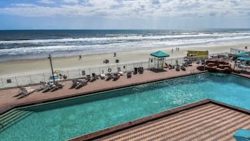 Uma área à beira da piscina com vista para a praia e o oceano, piscina cercada e cadeiras de descanso.