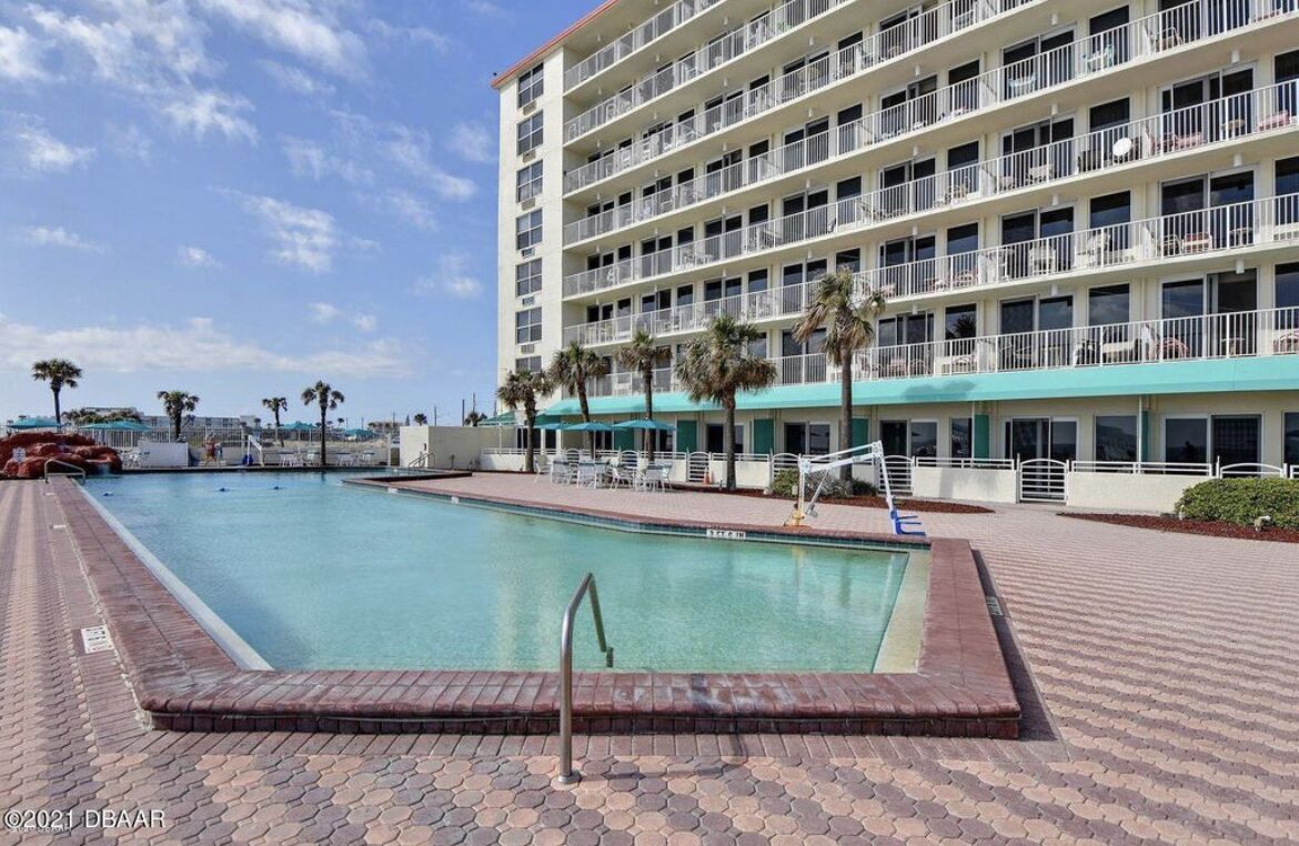 A hotel with a swimming pool, multiple balconies, and palm trees.