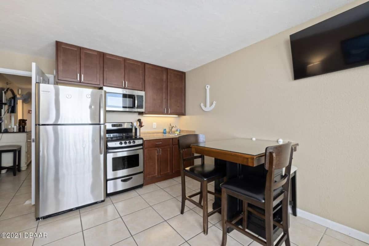 A compact kitchen with stainless steel appliances, wooden cabinets, and a dining area with two chairs.