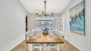 A dining area with a wooden table, white chairs, a chandelier, and a beach-themed painting. - Pool Home That Backs Up to Water- Only 20 Miles to Beautiful Florida Beaches! (Palmetto)