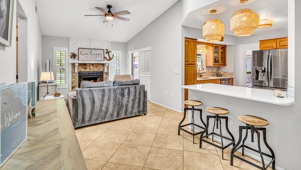 A modern kitchen with a white countertop, wooden cabinets, and a stainless steel refrigerator. There are three bar stools and a ceiling fan. - Pool Home That Backs Up to Water- Only 20 Miles to Beautiful Florida Beaches! (Palmetto)