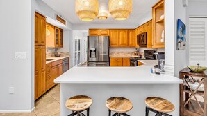 A modern kitchen with wooden cabinets, a stainless steel refrigerator, a large island with stools, and pendant lighting. - Pool Home That Backs Up to Water- Only 20 Miles to Beautiful Florida Beaches! (Palmetto)
