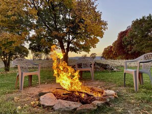 A campfire with chairs around it in a grassy area with trees in the background.
