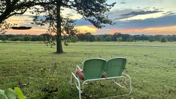 Een grasveld met een boom en twee groene stoelen eronder.