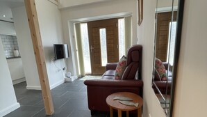 A spacious living area with a red sofa, a small wooden table, and a TV mounted on the wall. - Beautiful Robins Nest barn, Close to Minack, Porthcurno, Sennen, Sea ,beaches (Penzance)