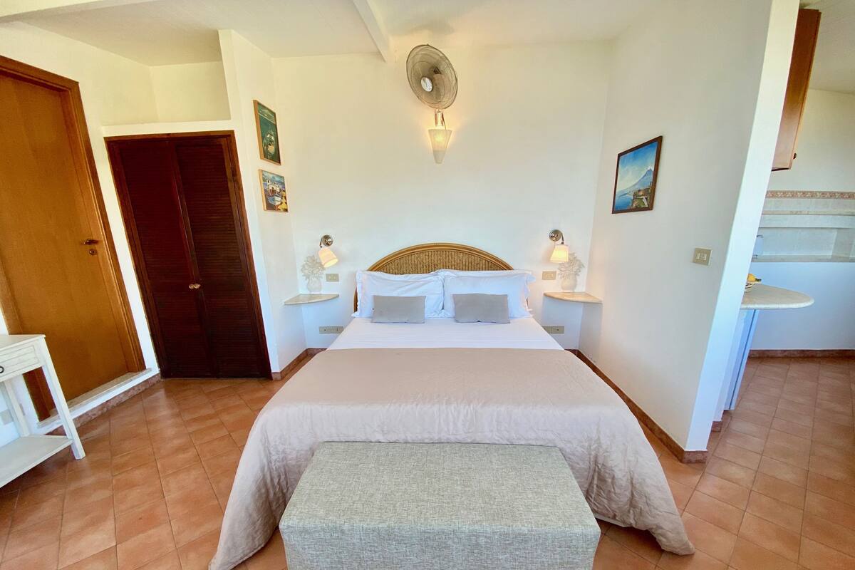 A bedroom with a large bed, bedside lamps, a nightstand, a bench, and a ceiling fan.