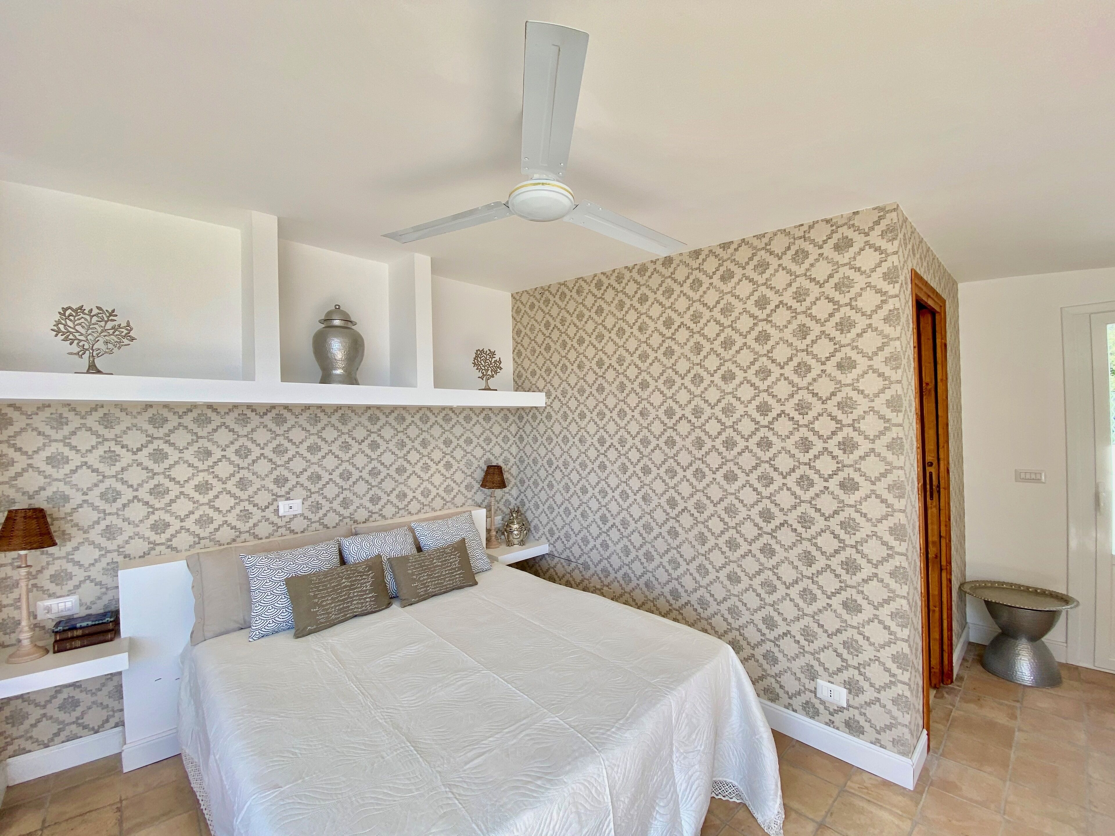 A bedroom with a bed, a ceiling fan, a nightstand, and a lamp.