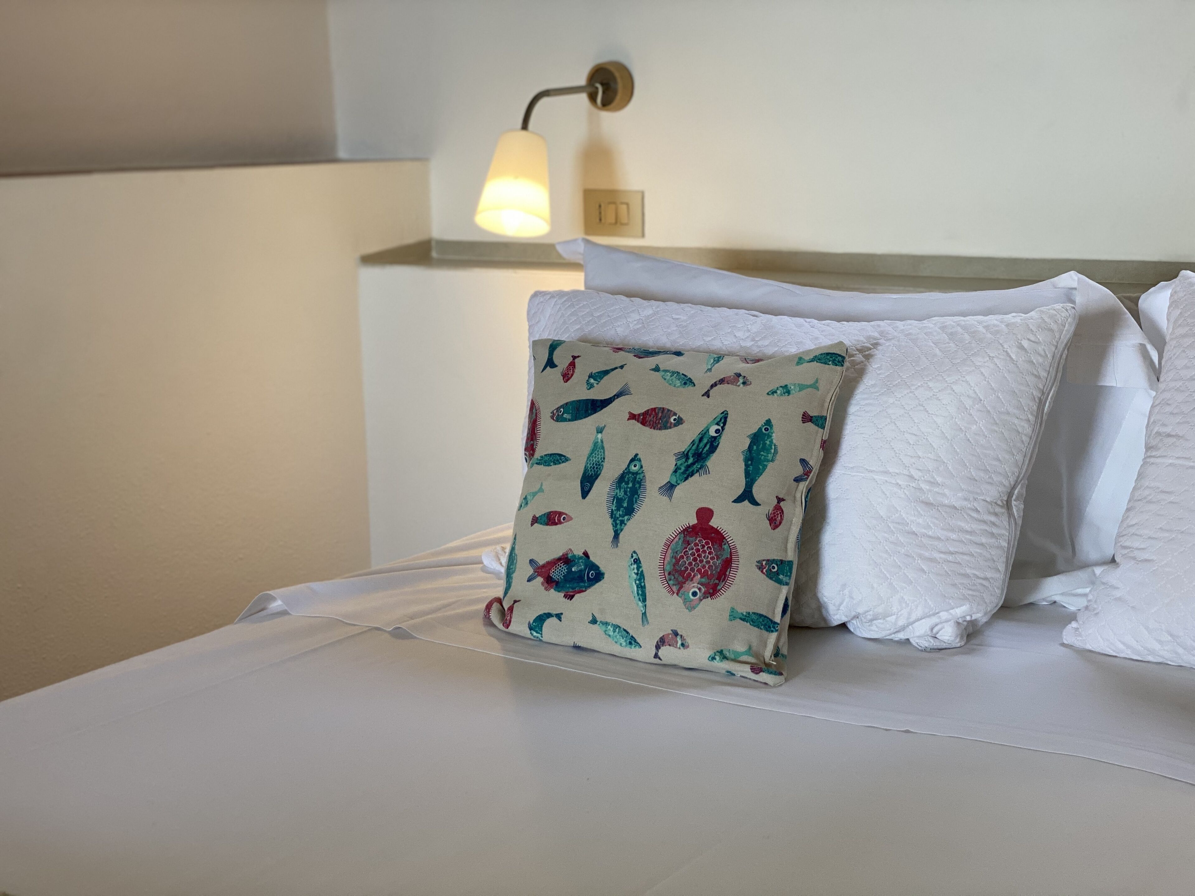 A neatly made bed with white linens and a decorative pillow featuring fish patterns.