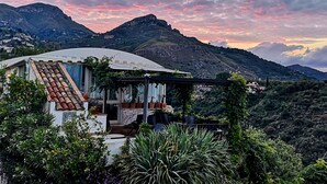A house with a curved roof, surrounded by lush greenery and purple flowers. - Residence Terra Rossa (Taormina)