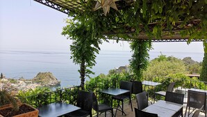 An outdoor patio with tables and chairs, overlooking a coastal view. - Residence Terra Rossa (Taormina)
