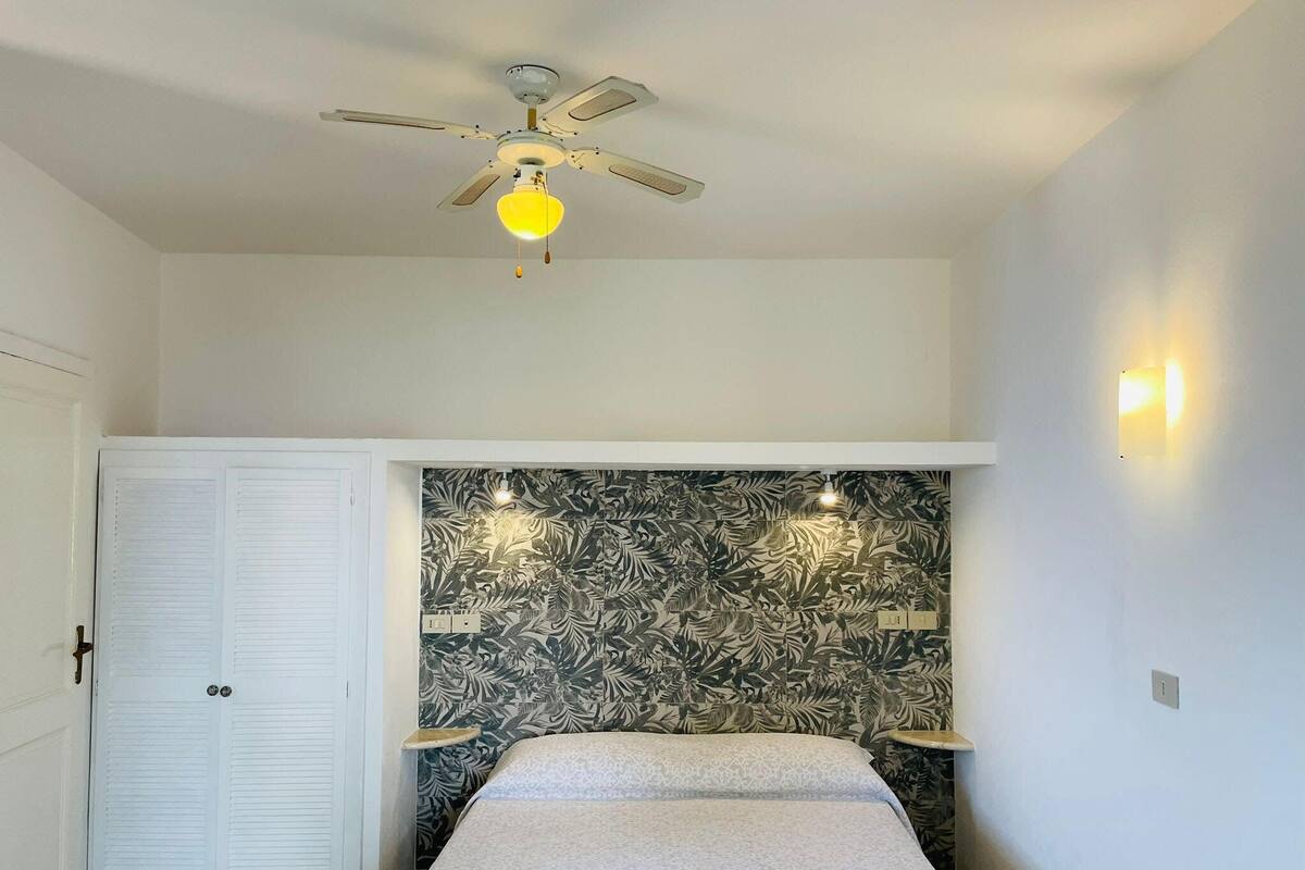 A bedroom with a bed, a ceiling fan, a wall-mounted light, and a door with a lock.