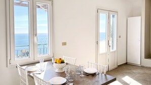 A dining area with a table set for four, white chairs, a bowl of fruit, and clear glasses. - Residence Terra Rossa (Taormina)